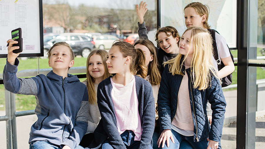 En grupp glada barn i en busskur tar en gruppselfie.