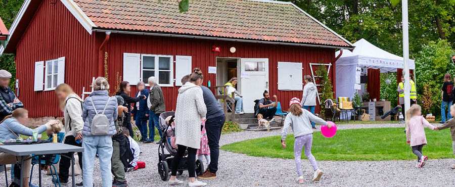 Människor på hembygdsgården. Det förekommer både barn och vuxna och ett tält med texten Återbrukat.