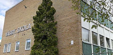 Bild på Väsby skolas fasad, en gul tegelvägg med texten Väsby skola.